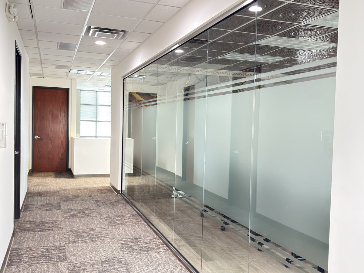 Modern office hallway with glass-walled offices and a wooden door with window wrap on conference room walls for privacy and decor